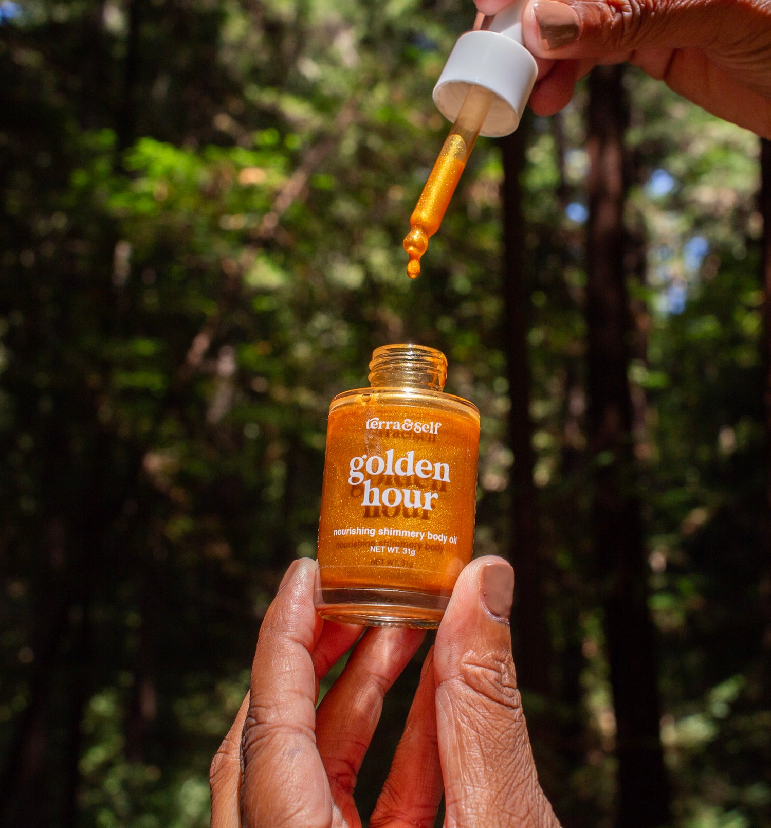 Woman holding up mini Golden Body Oil in forest