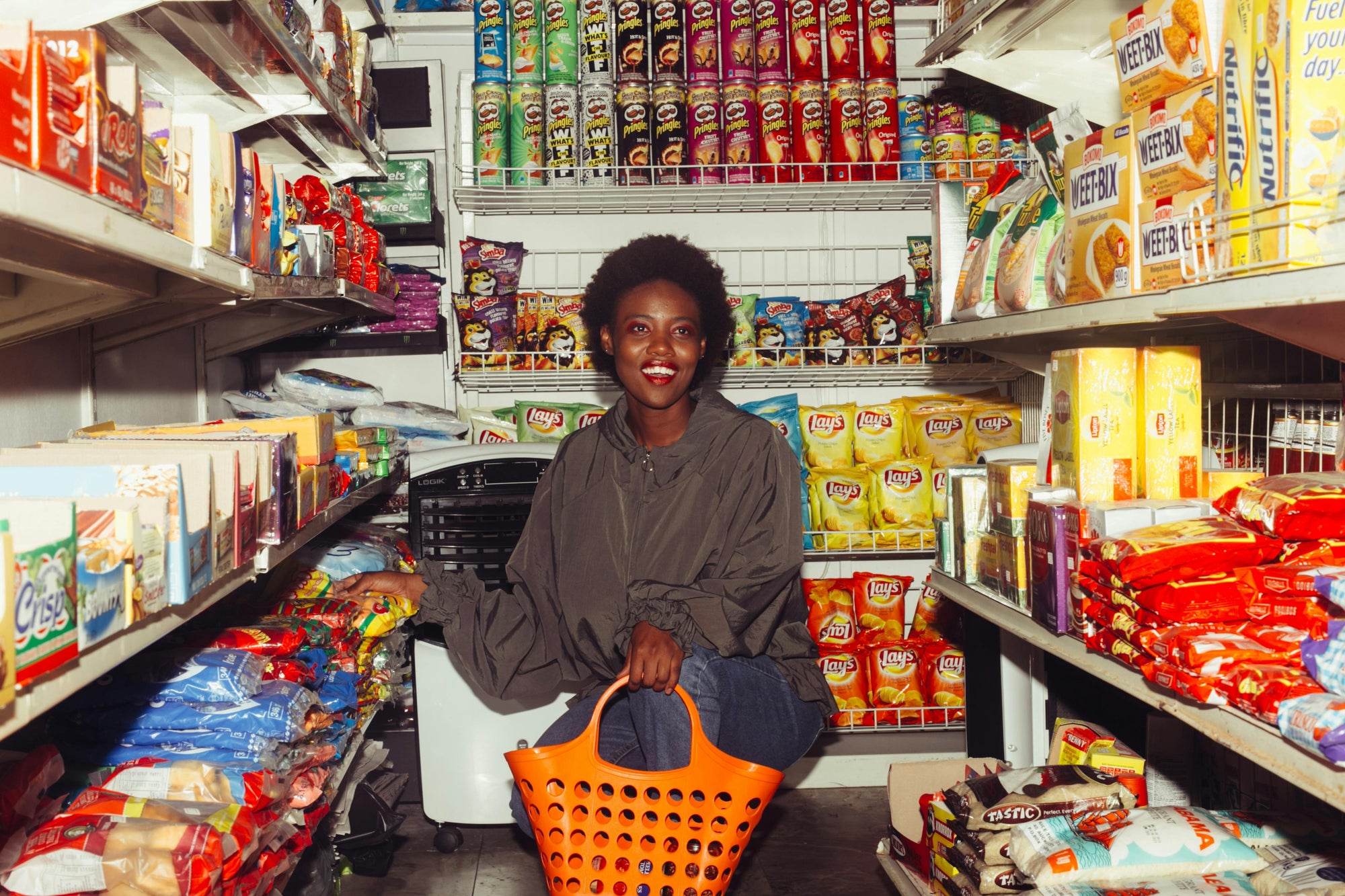 Smiling woman shopping with orange basket in snack and chips aisle at grocery store