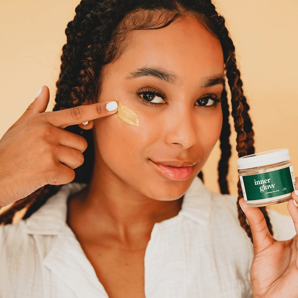 Acne Exfoliating Clay Mask shown by model holding it and placing some on face. The Inner Glow Clay Mask is formulated for acne prone skin by black owned skincare brand, Terra and Self.
