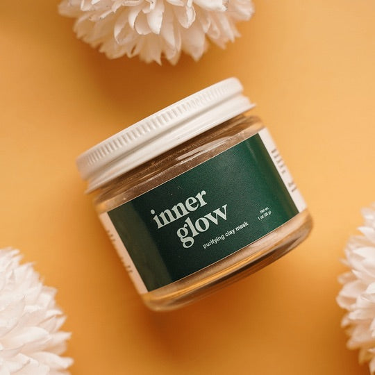 Acne Exfoliating Clay Mask, Inner Glow is shown against a yellow backdrop. This purifying clay mask is by Terra and Self, a sustainable beauty brand.